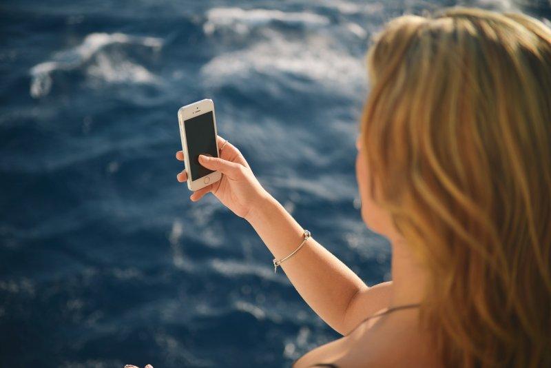 Die Abbildung zeigt eine Frau am Meer, in der Hand hält sie ein Smartphone